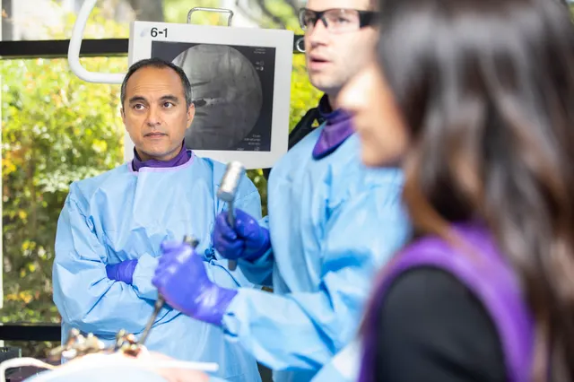 The instructor holds an instrument and looks toward the camera across the training station, attendees on either side.