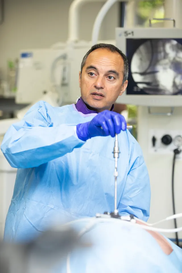 The instructor guides a driver into a training model, a fluoroscopy image of the lumbar spine on the monitor behind him.