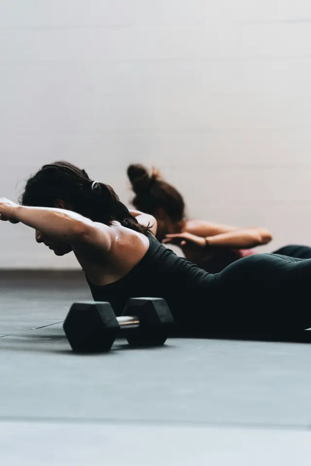 Two people lying face down on a gym floor, lifting their chest and arms clear of the mat