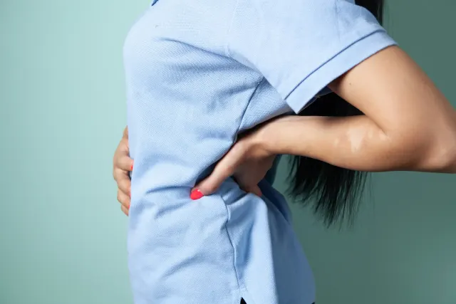 A person standing in profile with one hand pressed flat against their lower back