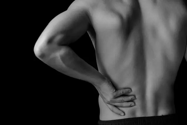 Black-and-white photograph of a person seen from behind, pressing a hand into their lower back
