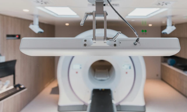 A ring-shaped medical scanner with its couch extended, beneath a suspended overhead panel