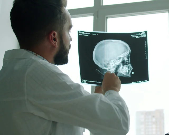 A clinician holds an X-ray film up to a window, studying it