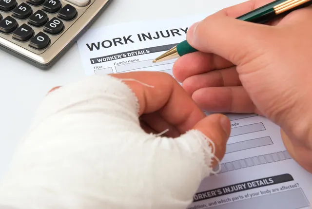 A person with a bandaged hand filling in a work injury claim form