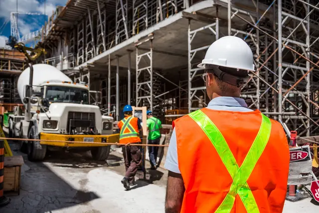 A construction worker in a hard hat and high-visibility vest looks out over an active building site